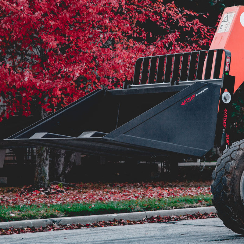 Arrow fork mounted bucket carried on an orange telehandler with a bar load backrest above it, the fork pockets visible under the bucket floor and a red Arrow decal on the side plate