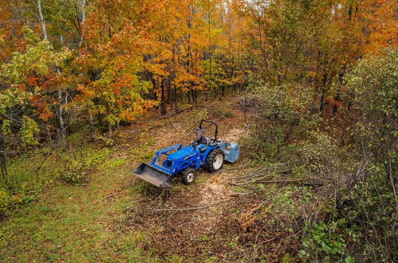 Aerial view of a blue tractor clearing brush with the MP348 on a slope among orange autumn maples