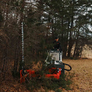 Sickle bar mower cutting into dense evergreen brush from a white Bobcat mini track loader, with the bar buried in the foliage