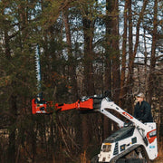 Sickle bar mower reaching up into pine branches with the arm extended from a white Bobcat MT100 mini track loader