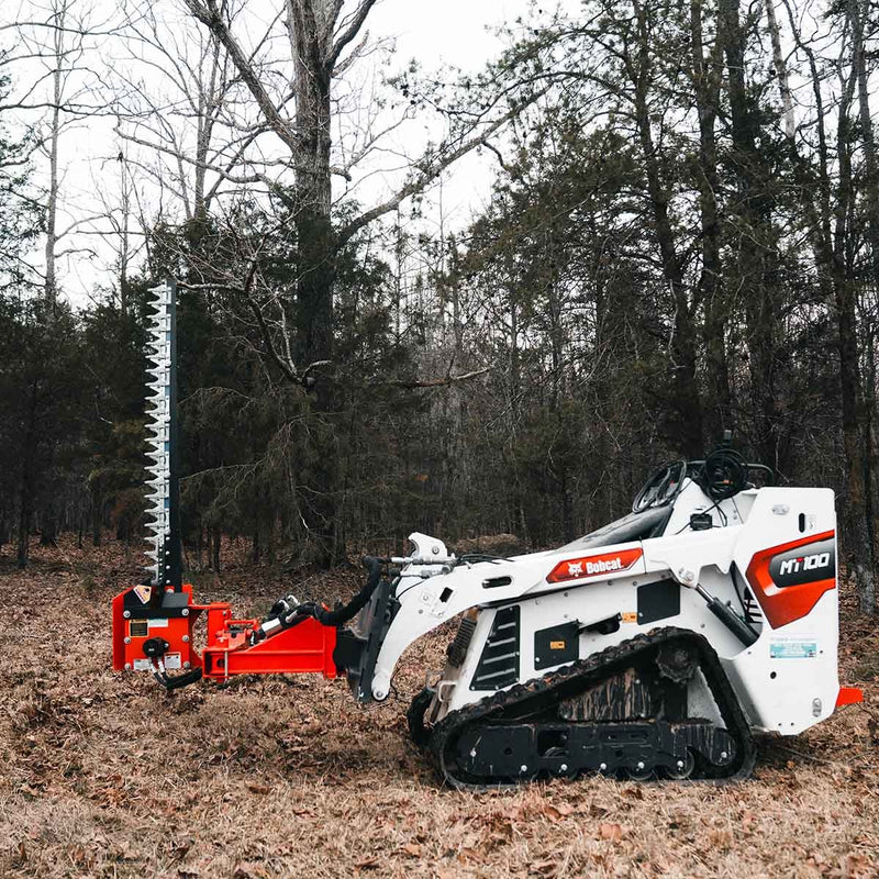 Full side view of a white Bobcat MT100 mini track loader carrying the Eterra sickle bar mower with the bar raised vertically, on leaf litter in open woodland