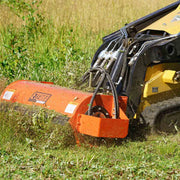 Orange Sidewinder flail mower cutting tall grass on a yellow tracked mini skid steer, with the hose bundle and flat-faced couplers visible at the mount