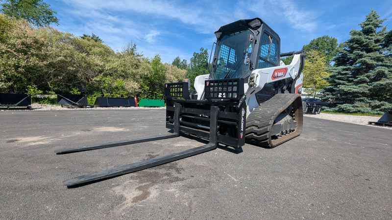 Glacier hydraulic pallet forks mounted on a compact track loader, forks extended forward on a paved lot