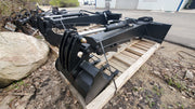Glacier backhoe attachment strapped to a pallet outdoors, showing the boom, cylinder, thumb, and bucket