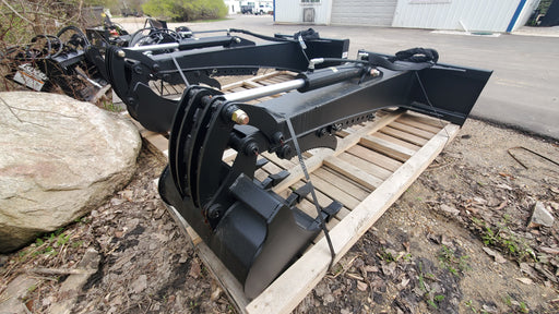 Glacier backhoe attachment strapped to a pallet outdoors, showing the boom, cylinder, thumb, and bucket