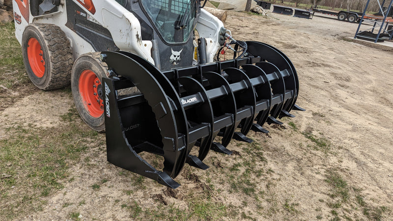 Glacier Extreme rake and brush grapple beside a skid steer, angled view down the length of the tine bar