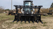 Glacier Extreme rake and brush grapple on a skid steer in a wooded clearing, front view of the wide clam