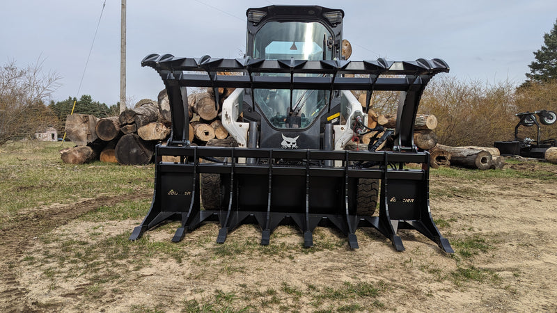 Glacier Extreme rake and brush grapple on a skid steer in a wooded clearing, front view of the wide clam