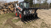 Glacier Extreme rake and brush grapple on a skid steer by a stack of logs, three-quarter view with the clam open