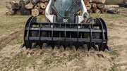 Glacier Extreme rake and brush grapple on a skid steer with a log pile behind, head-on view across the tines