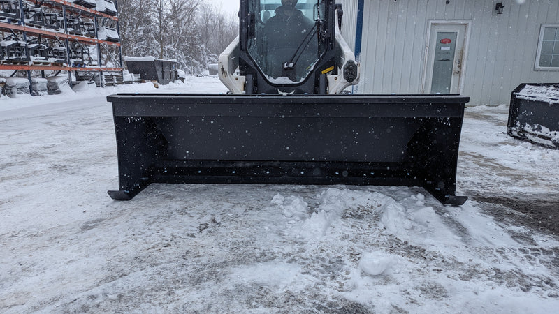 Glacier HD snow pusher on a skid steer by a building in winter, head-on view of the full moldboard width