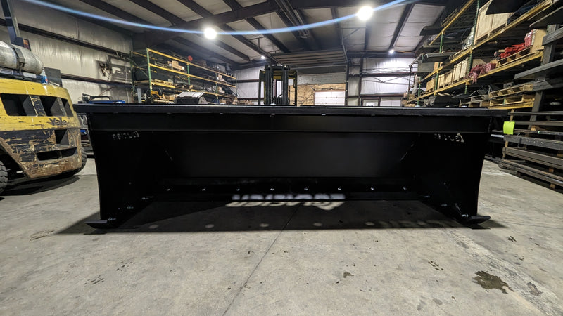Glacier HD snow pusher in a shop, straight-on front view across the full moldboard and the shoe plates