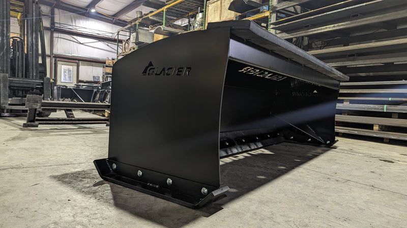 Glacier HD snow pusher in a shop, angled view showing the boxed side plate and the bolted cutting edge