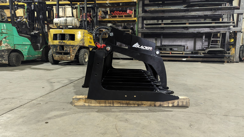 Glacier root and brush grapple on a loader, three-quarter view showing the reinforced frame and cylinder guards