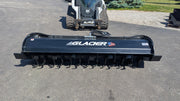 Glacier rotary tiller head-on behind a compact track loader, showing the full working width and the tine rotor