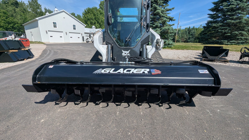 Glacier rotary tiller mounted on a Bobcat track loader outdoors, straight-on view across the tilling drum