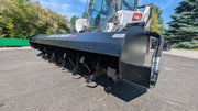 Glacier rotary tiller on a track loader, low angled view along the drum showing the tilling teeth and the side skid