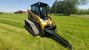 Glacier Extreme Stump Shark mounted on a yellow compact track loader in a grass field, arm extended forward