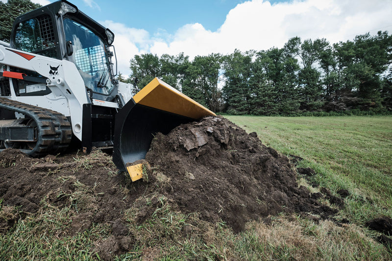 HitchDoc 6-Way Dozer Blade pushing a pile of dark soil across grass, three-quarter view with the moldboard loaded and the yellow top rail visible
