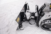 Close overhead view of the HitchDoc mini skid steer angle blade mount end, showing both trip springs, the angling cylinder, the quick connect hydraulic couplers, the yellow warning decal and the skid shoe below