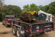 HitchDoc Push-Off Bucket carrying a heaped load of clay and sod over the side of a dump trailer, the yellow extractor just starting its stroke