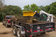 HitchDoc Push-Off Bucket with the extractor blade driven fully forward, material breaking up and falling into a dump trailer behind a pickup