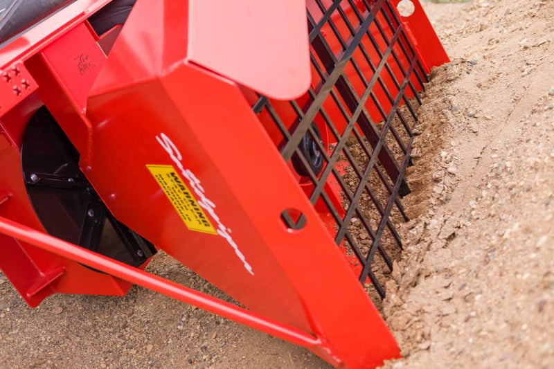 HitchDoc Sandpiper tipped down into a pile of sand to self-load from the seat, low angle showing the hopper wall, the grate along the top edge and the spreader disc
