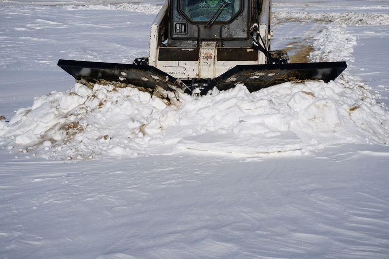 HitchDoc V-Blade in the V-cut position seen head-on from the front, both wings swept back on a skid steer with snow rolling off each end