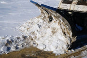 HitchDoc V-Blade in the scoop position carrying a full load of snow, side view with the rolled moldboard and the top blade extension holding the load