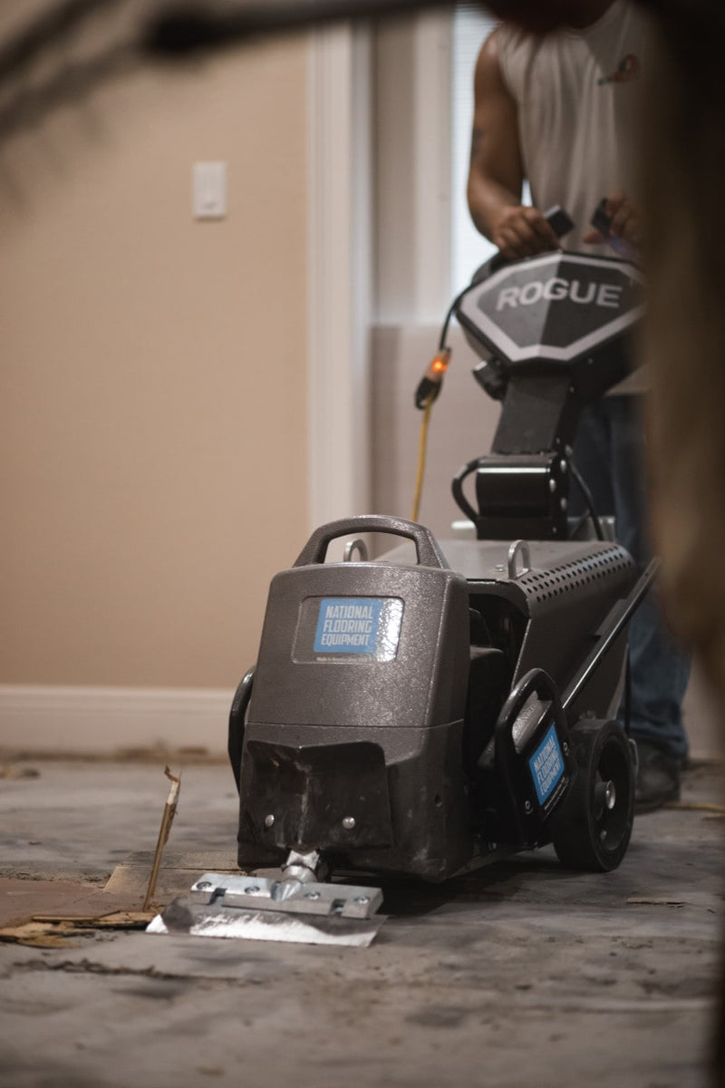 Rogue walk-behind scraper on a stripped subfloor with an operator behind it and ROGUE badged on the panel