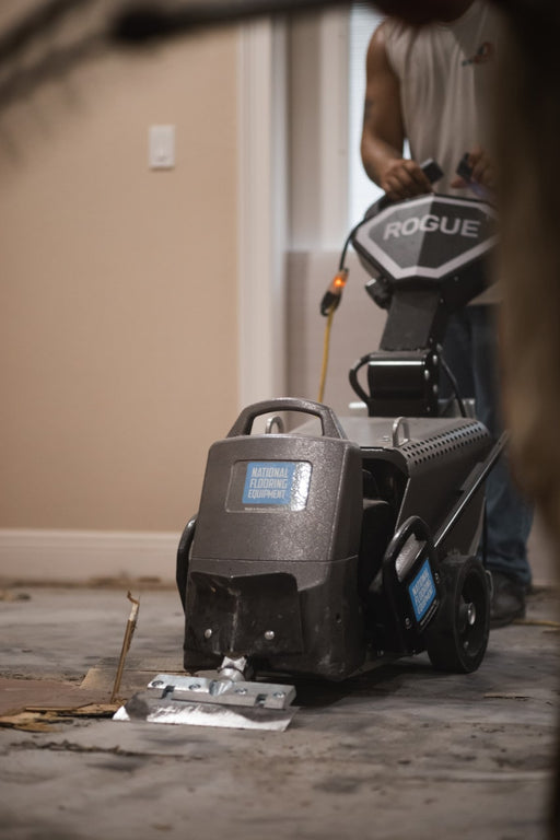 Rogue walk-behind scraper on a stripped subfloor with an operator behind it and ROGUE badged on the panel