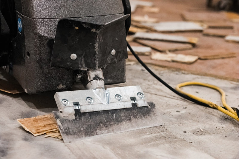 Rogue walk-behind scraper blade holder and wide blade at floor level on a stripped concrete slab