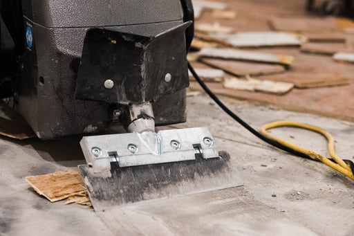 Rogue walk-behind scraper blade holder and wide blade at floor level on a stripped concrete slab