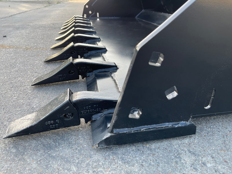 Close-up along the tooth bank of the extreme duty bucket, showing the tooth shanks and the side plate mounting holes
