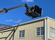 Trash hopper lifted above a metal building roof on the boom