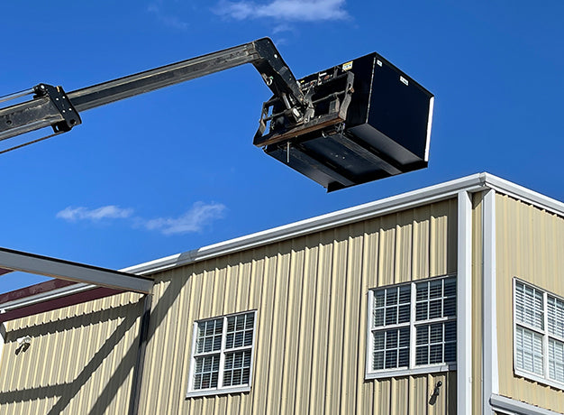 Trash hopper lifted above a metal building roof on the boom