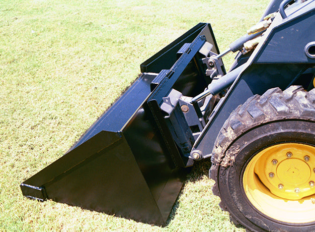 Heavy duty skid steer bucket tipped forward on a loader, showing the low profile and cutting edge