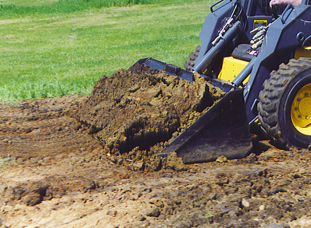Heavy duty skid steer bucket cutting into a soil pile alongside a lawn