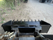 Heavy duty skid steer bucket viewed from the operator's seat over the loader arms and hoses