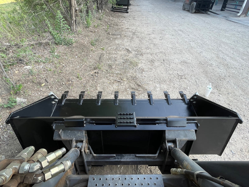 Heavy duty skid steer bucket viewed from the operator's seat over the loader arms and hoses