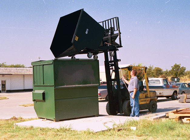 Forklift emptying the hopper over a dumpster in a yard