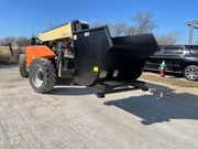 Telehandler carrying the self-dumping hopper on its forks across a yard