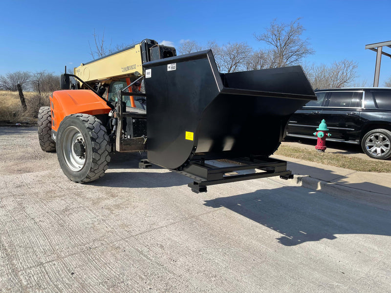 Telehandler carrying the self-dumping hopper on its forks across a yard