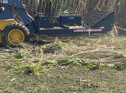 Brush cutter working on a skid steer over a windrow of cut cane