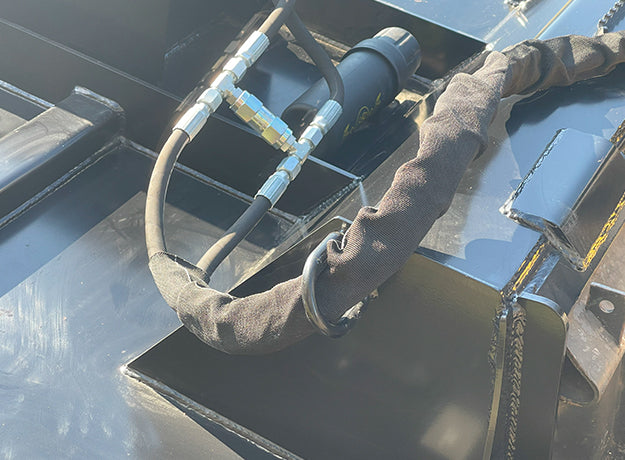 Close-up of the brush cutter's hydraulic couplers and hoses in their protective sleeve