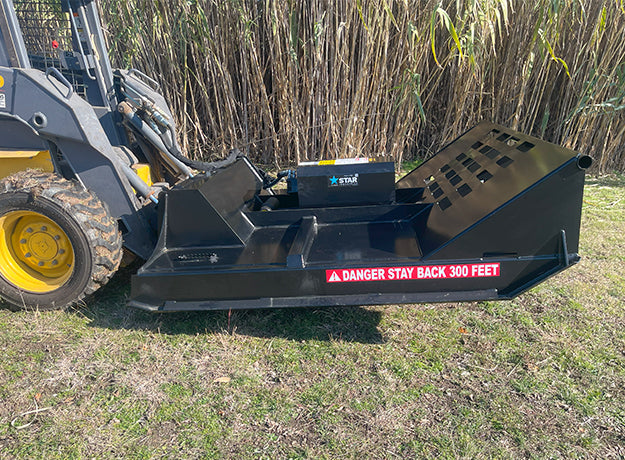 Brush cutter on a yellow skid steer parked in front of standing cane