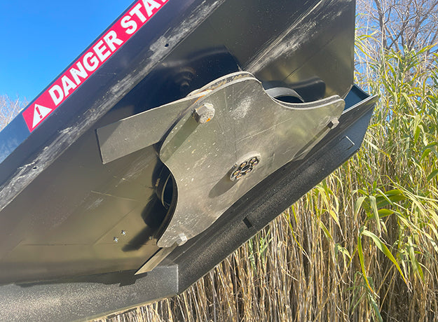 Underside of the brush cutter deck showing the blade carrier hub behind the front skirt