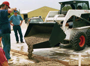 Skid steer placing concrete from the bucket into a formed pad while two workers watch