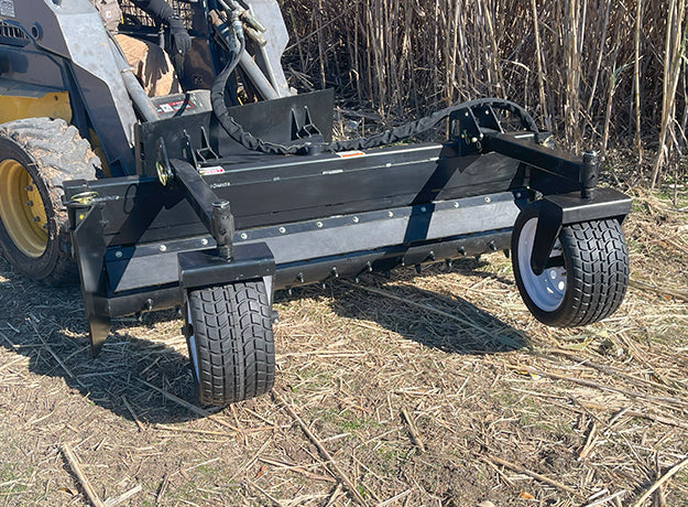 Full-length side view of the power rake mounted on a yellow skid steer