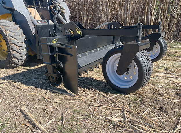 Power rake on a skid steer working cut ground, the removable side plate and gauge wheel in view